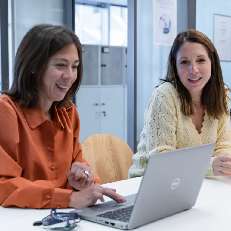 Photo de deux collaboratrices du groupe InVivo en train de sourire et de regarder l'écran d'un ordinateur portable dans un bureau.